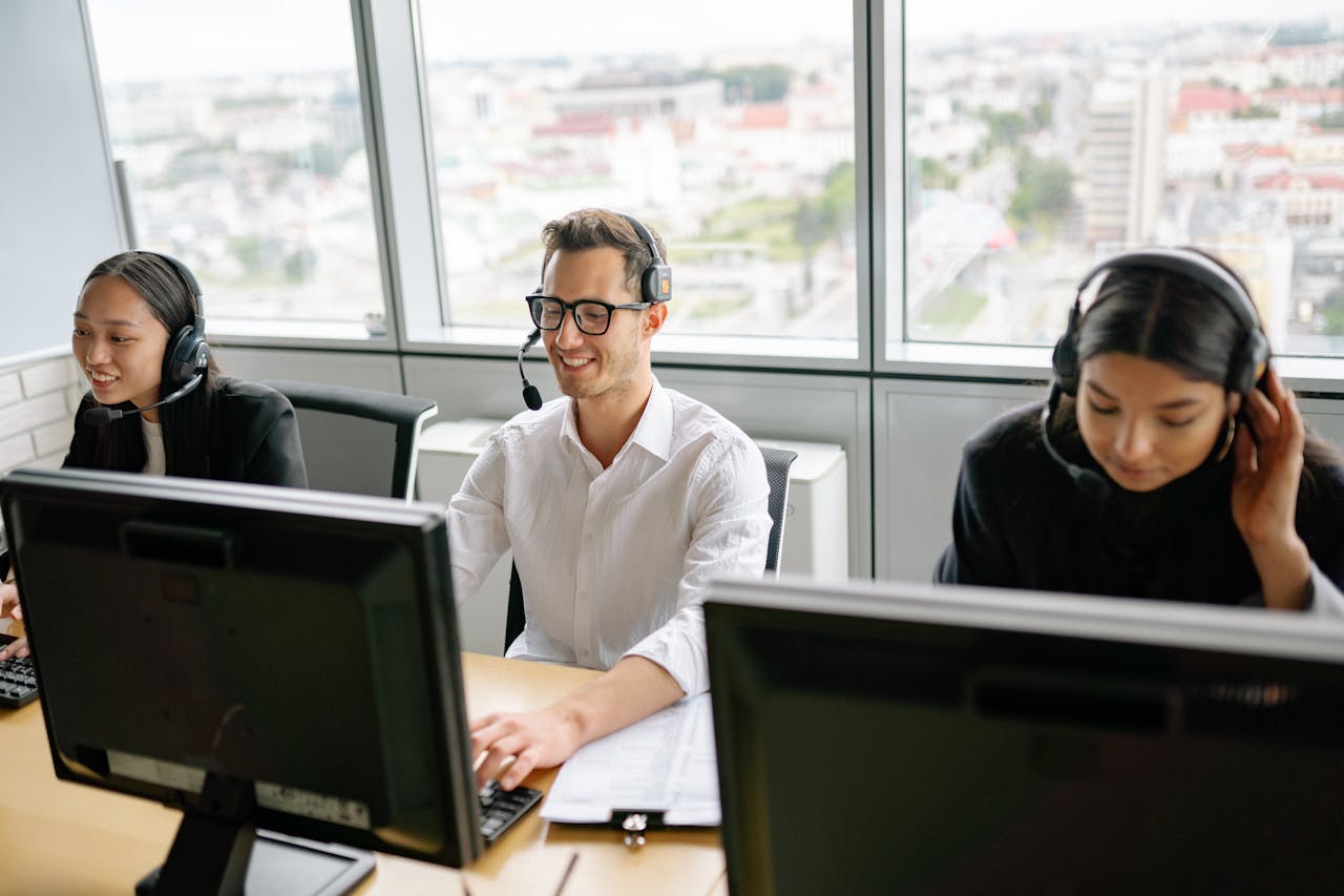 Group of call center employees wearing headsets, collaborating in a bright office environment.